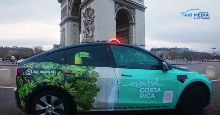 Un taxi arborant un wrap aux couleurs du Costa Rica circule devant l'iconique Arc de Triomphe à Paris, France.