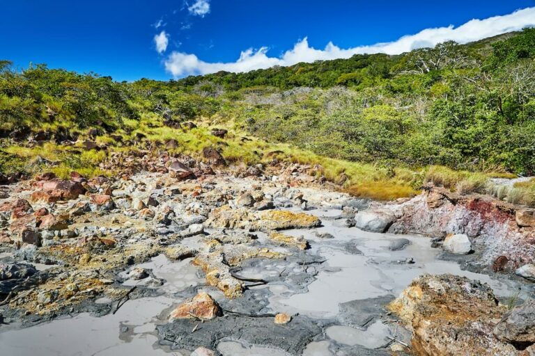 Un paysage époustouflant du Rincón de la Vieja, avec un ciel bleu, des nuages blancs, une végétation verte luxuriante et du lodo volcanique.